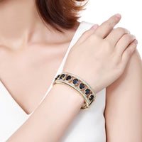 Side angle view of KHAISTA blue crystal gold bangle