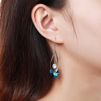 Side angle view of KHAISTA blue heart crystal drop earrings