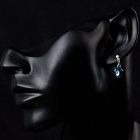 Side angle view of KHAISTA dark blue crystal heart drop earrings