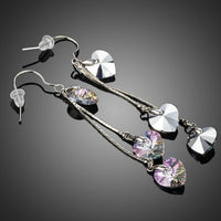 Side angle view of KHAISTA dangling heart crystal drop earrings