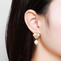 Side angle view of KHAISTA geometric pearl waterdrop dangle earrings