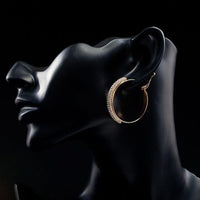 Side angle view of KHAISTA gold plated bangle design drop earrings