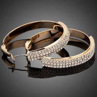 Close up of KHAISTA gold plated bangle design drop earrings