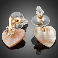 Close up of KHAISTA gold plated light peach crystal heart earrings