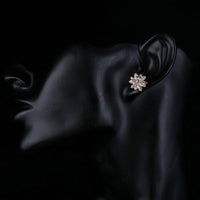 Side angle view of KHAISTA gold plated CZ flower shaped stud earrings