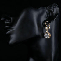 Side angle view of KHAISTA gold plated CZ love drop earrings