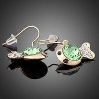 Close up of KHAISTA gold plated green crystal fish drop earrings