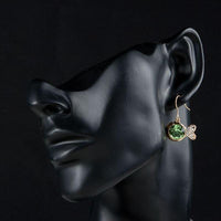Side angle view of KHAISTA gold plated green crystal fish drop earrings