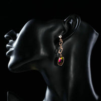 Side angle view of KHAISTA gold plated curved crystal drop earrings