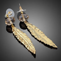 Close up of KHAISTA gold plated leaf drop earrings
