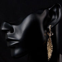 Side angle view of KHAISTA gold plated leaf drop earrings