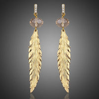 KHAISTA gold plated leaf drop earrings on white background