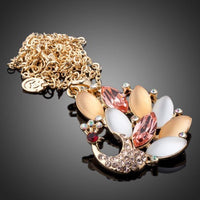 Side angle view of KHAISTA gold crystal peacock pendant necklace