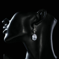 Side angle view of KHAISTA heart design oval crystal drop earrings