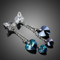 Side angle view of KHAISTA ocean blue crystal heart drop earrings