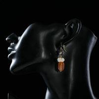 Side angle view of KHAISTA pumpkin orange crystal drop earrings