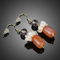 Close up of KHAISTA pumpkin orange crystal drop earrings
