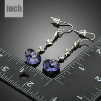 Side angle view of KHAISTA purple heart design crystal drop earrings