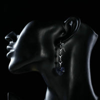 Close up of KHAISTA purple heart design crystal drop earrings