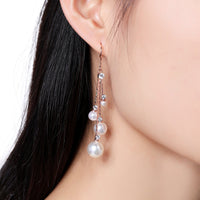 Side angle view of KHAISTA pearl chain dangle hook earrings
